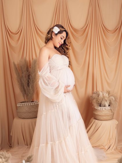 A full-length portrait in a dreamy, bohemian-style white gown with puffy sleeves, set against a neutral backdrop.