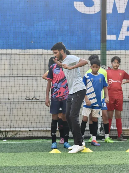 A coach demonstrating a drill to a group of young football players. My training sessions are hands-on, with coaches actively participating to ensure techniques are taught correctly.