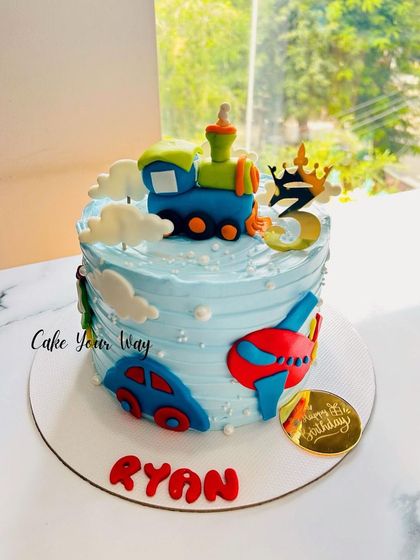 A cute vehicle-themed cake with a train, car, and airplane, perfect for a little boy's 3rd birthday.