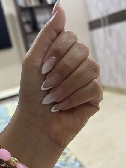 A simple yet elegant ombre French manicure on sharp, stiletto-shaped nails, blending a natural base into a soft white tip.