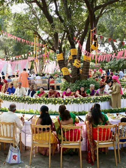 A wide shot of a large Pangat setup under a beautiful old tree. This image captures the scale and festive atmosphere of the event, with guests seated together to enjoy a traditional Maharashtrian feast.