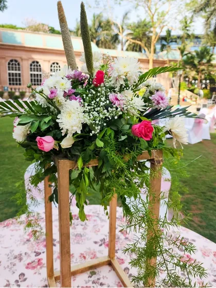 A beautiful floral centerpiece on a wooden stand, perfect for an outdoor garden wedding, featuring a mix of pastel flowers and fresh greenery.