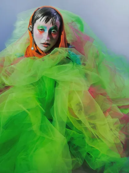 The model is enveloped in layers of neon green tulle, creating a cocoon-like effect. This image plays with volume and transparency to evoke a sense of metamorphosis.