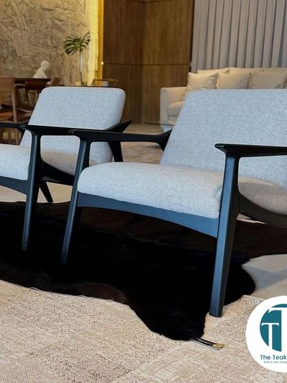 A pair of sleek, mid-century modern lounge chairs made from teakwood with a black finish. The light grey upholstery provides a beautiful contrast, creating a sophisticated look perfect for a formal living room.
