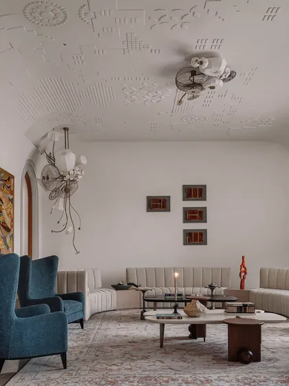 The ceiling of this formal living room is adorned with jewel-like light fixtures that resemble blooming flowers. These intricate, sculptural lights create a canopy of art, complementing the custom gypsum embroidery on the ceiling.