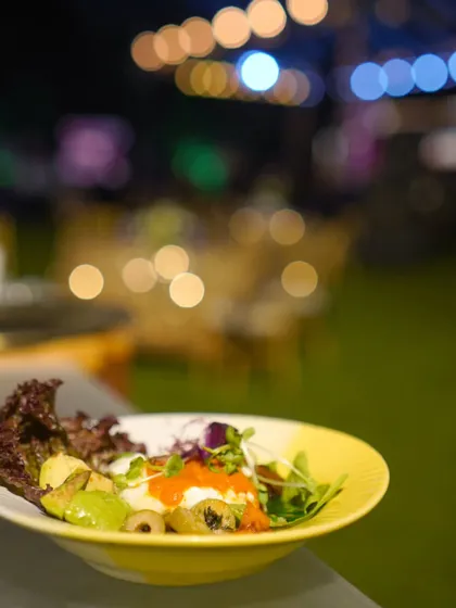 Our Chipotle Bowl is a vibrant and healthy option for any event. Served here against the backdrop of an evening party, it combines fresh greens, beans, corn, and other toppings for a customizable and flavorful meal.