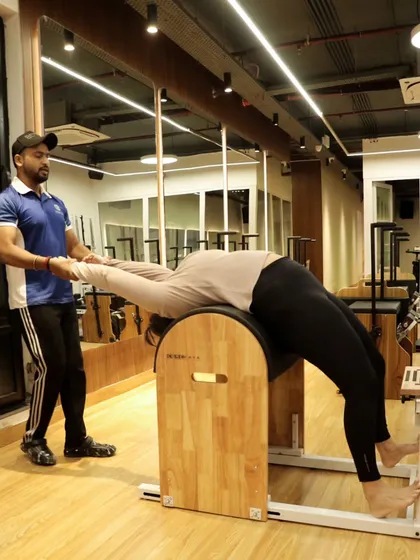 This image shows a coach providing support as a client performs a full-body stretch on the ladder barrel, emphasizing our commitment to safe and effective training.
