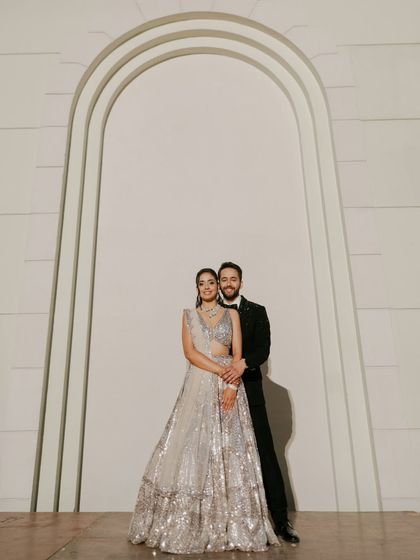 An elegant and classic Sangeet portrait. The couple stands against a minimalist backdrop, letting their stunning outfits and confident connection take center stage.