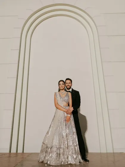 An elegant and classic Sangeet portrait. The couple stands against a minimalist backdrop, letting their stunning outfits and confident connection take center stage.
