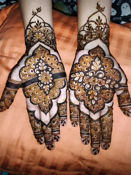 This design features a prominent mandala on the back of the hand, a classic element in henna art. The surrounding patterns use negative space to make the central design truly pop.