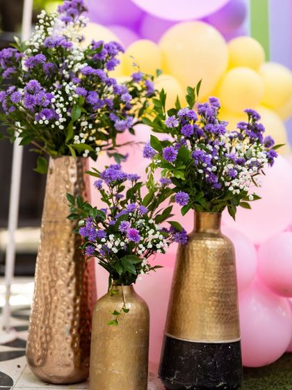 I also do birthdays! For Ayra's first birthday, I created this colorful setup with purple flowers in golden vases against a backdrop of pink and yellow balloons, bringing a rainbow theme to life.