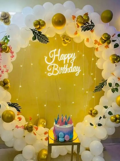 An elegant birthday setup in white and gold. The circular balloon arch is accented with fairy lights and leaf details, creating a sophisticated look for any celebration.
