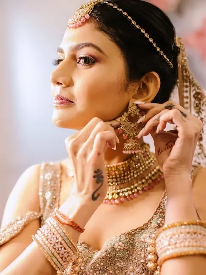 A close-up of the bride getting ready. This shot captures the application of her jewelry, which complements the dewy makeup and subtle glittery eye look.