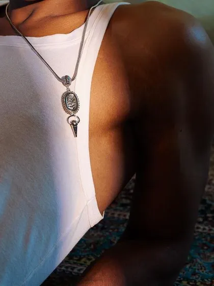 A detailed close-up from the Amama Jewels PhotoVogue series. The focus is on the pendant against the simple white tank top, highlighting the product in a natural setting.