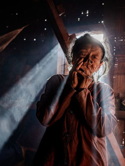 An Apatani woman in Ziro Valley, caught in a ray of light inside her home. This environmental portrait captures her in her daily life, highlighting the unique traditions of her tribe.