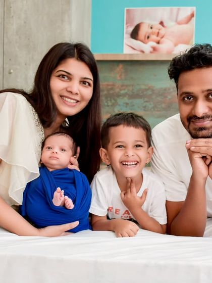 A bright and happy portrait of a family of four relaxing together on a bed. This lifestyle approach captures genuine smiles and the relaxed, joyful atmosphere of being at home with a new baby.