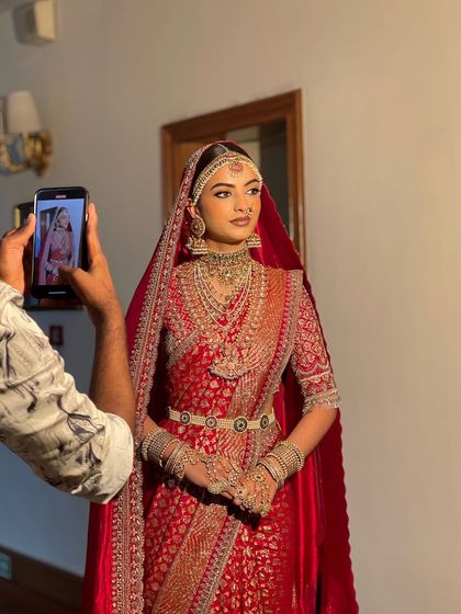 A behind the scenes moment, capturing the bride's full look. Her sleek low bun is perfectly set under the dupatta, ensuring a neat and polished appearance for the wedding ceremony.
