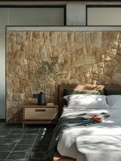 A bedroom in 'Antriya' features a beautiful random rubble stone wall, bringing a raw, natural texture to the otherwise minimalist interior.