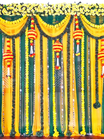A traditional backdrop for a Dohale Jevan or Haldi function, using green and yellow drapes, marigold strings, and hanging floral tassels.