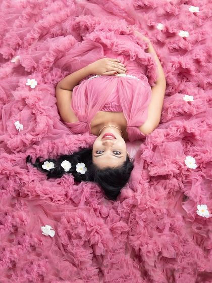 A lovely "sleeping beauty" pose, looking up at the camera with a sweet smile. The bed of pink ruffles creates a soft and whimsical frame around her.