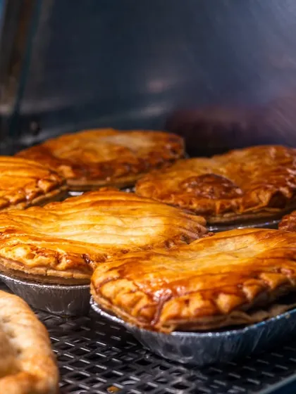 A tray of savory pies with golden, flaky crusts. The warm lighting and tight crop make them look comforting and delicious.
