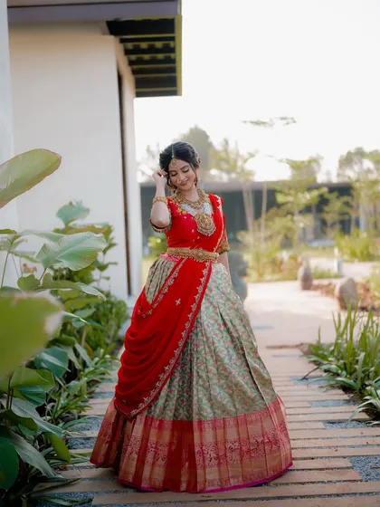 A full-length shot of actress Niveditha Gowda in a traditional half saree. The garden path creates leading lines that draw the eye to the beautifully designed outfit.