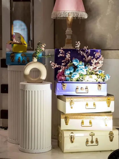 Vintage-style trunks in pastel colors, stacked and filled with flowers, create a chic and thematic decor accent. These details help build a rich, layered look.