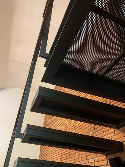 A detail of a modern staircase with perforated metal treads and a simple steel stringer, set against an exposed brick wall. This combination of industrial and rustic materials creates a rich textural contrast.