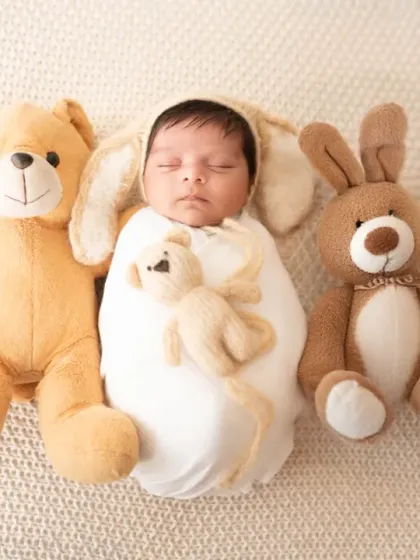 A sweet newborn with bunny ears sleeps soundly, cuddled by a line of teddy bears. This playful setup is perfect for creating a cute and memorable portrait.