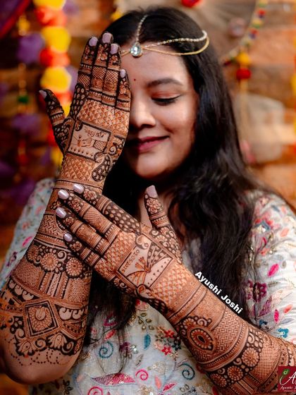 A beautiful, professionally shot photo of the bride showcasing her intricate mehendi, which includes wedding dates and ritual scenes.