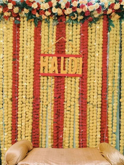 A classic Haldi backdrop for a home function, made entirely of yellow and red marigold flower strings with a custom "Haldi" sign.