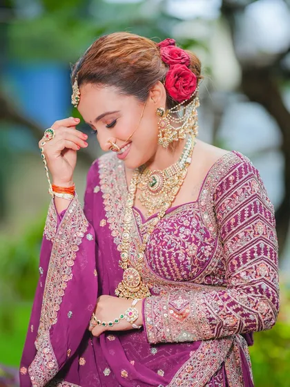 A candid moment of bridal happiness. The soft lighting highlights the glowing skin and the intricate details of her jewelry, while the red roses in her bun add a classic romantic touch.