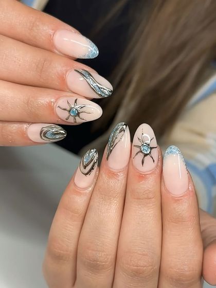 A cool-toned summer nail set with a light blue glitter French tip and abstract silver chrome sun and wave designs.