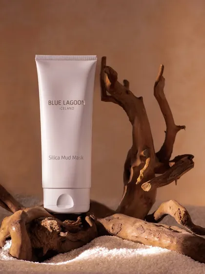 A silica mud mask placed on a piece of driftwood against a sandy, textured background. The earthy tones and natural elements give this shot a raw and organic feel.