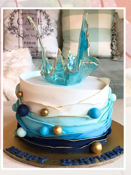 An abstract ocean-themed cake with blue ombre waves, gold accents, and a striking blue sugar sail on top.