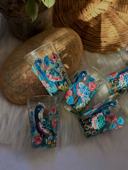 The 'Mor Pankh' peacock tea glasses scattered on a soft fur rug, showing off their vibrant colors.