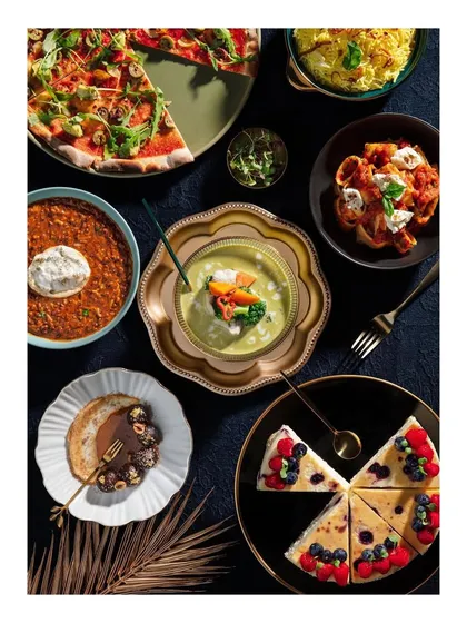 A vibrant flat lay showcasing a multi-cuisine spread from Club Jolies. The composition includes pizza, pasta, soup, and desserts, demonstrating the wide variety of delicious options available on their menu.