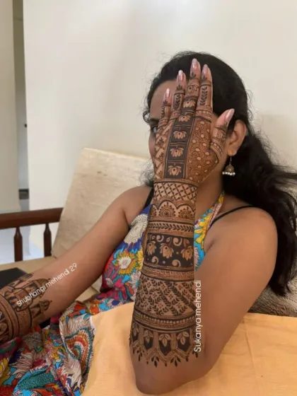 A bride showcasing her full-arm mehendi. The design features bold bands with lotus motifs and intricate filler patterns, creating a stunning visual effect.