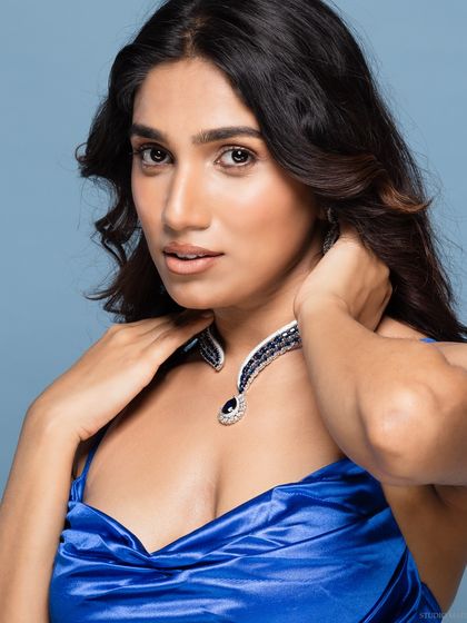 A soft and engaging portrait of the model, with her hand gently touching her neck.