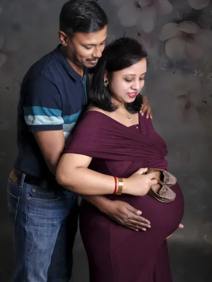 A classic maternity pose with the couple holding tiny shoes on the baby bump. The dark, painterly backdrop adds a touch of timeless elegance.