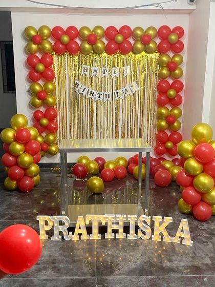A simple and traditional birthday decoration with a foil curtain backdrop. The red and gold balloon frame is a classic choice for a vibrant celebration.