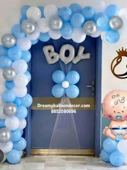 A cute 'BOY' themed entrance decoration for a welcome home party. The blue and white balloon arch is accented with a 'BOY' foil balloon and a baby-shaped balloon pillar.