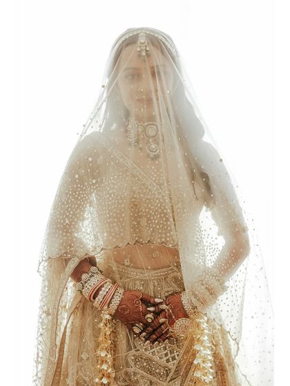 A breathtaking bridal portrait. The bride looks ethereal behind her sheer, embellished veil, a key piece that adds a layer of traditional mystique to her modern Tarun Tahiliani lehenga.