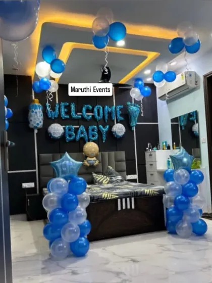 A 'Welcome Baby' room decoration in blue and white. The setup includes 'Welcome Baby' foil letters over the bed, balloon columns, and balloons on the ceiling.