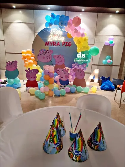 This photo captures the party atmosphere of the Peppa Pig theme, with themed party hats on the table in front of the main decoration backdrop.
