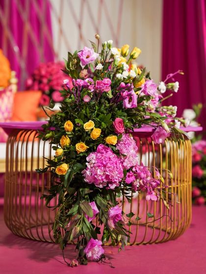 A stunning floral arrangement featuring pink hydrangeas and yellow roses cascading over a golden wire-frame table.