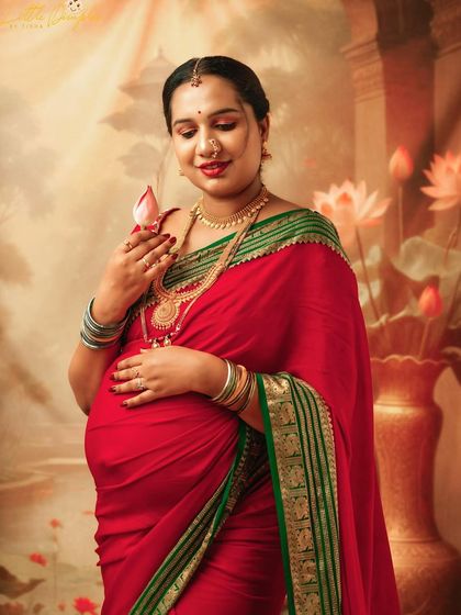 A close-up portrait of a glowing mom-to-be in a red saree, holding a lotus flower. The details in her jewelry and the soft lighting make this image so special.