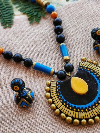 An elegant semi-circular pendant necklace with a simple long chain of black and colored beads. This set, in black, blue and gold, comes with a cute matching jhumka.