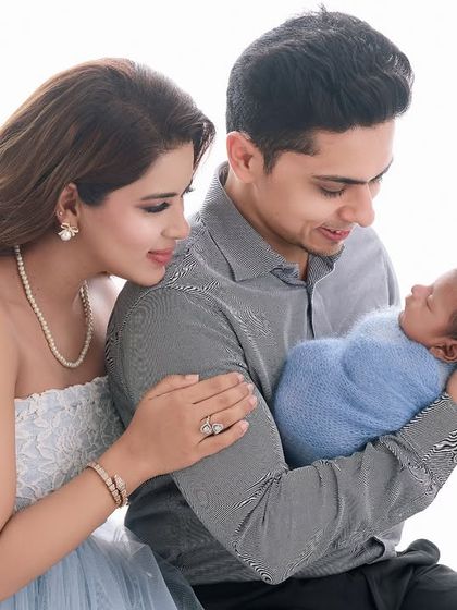 A glowing mother and father admire their newborn, who is wrapped in a soft blue swaddle, creating a bright and joyful family photograph.