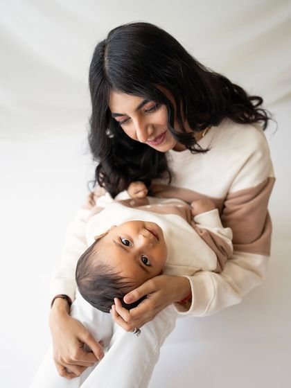 A mother looking down lovingly at her baby. The simple white backdrop ensures all the attention is on this tender, quiet moment.